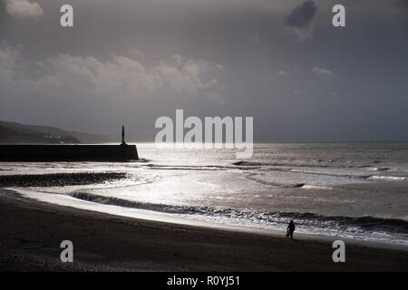 Aberystwyth, Wales, UK. 8. November 2018. UK Wetter: Dunkel brütende stürmischen Himmel über Menschen zu Fuß am Strand entlang in Aberystwyth, da das Wetter wieder versammeln sich nass und windig. Das Met Office haben eine gelbe Warnmeldung für starken Wind, starker Regen und die Wahrscheinlichkeit, dass der Fluss- und Küstengebieten für große Teile von South Wales und dem Westen des Landes morgen Credit: Keith Morris/Alamy Live Neuigkeiten Stockfoto