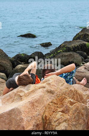 Ein junges Paar Festlegung auf den Felsen Sprechen, Denken, und genießen Sie einfach das Ende der Tag am Strand. Stockfoto