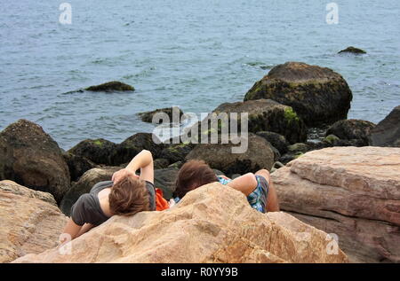 Ein junges Paar Festlegung auf den Felsen Sprechen, Denken, und genießen Sie einfach das Ende der Tag am Strand. Stockfoto