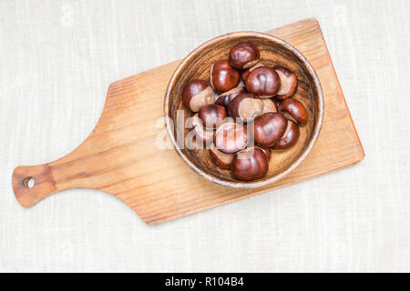 Stapel von Aesculus hippocastanum oder conker Nüsse in der Platte auf Schneidebrett auf Tischdecke. Stockfoto