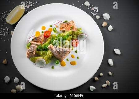 Gebratener Lachs auf weiße Platte auf dunklem Hintergrund angeordnet Stockfoto