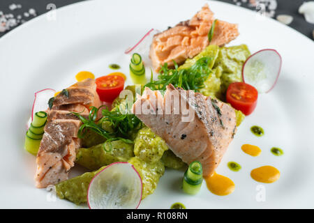 Gebratener Lachs auf weiße Platte auf dunklem Hintergrund angeordnet Stockfoto