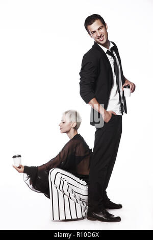Fröhlicher Kerl in einem schwarzen Anzug und einem Mädchen auf weißem Hintergrund verspielt, Tanzen mit Kaffeetassen. Kaffee trinken gehen. Werbung. Stockfoto