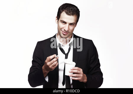 Ein junger Mann in einem schwarzen Anzug hält eine Tasse Kaffee mit Schlagsahne. Werbung, Kreativität. Kaffee trinken gehen. Stockfoto