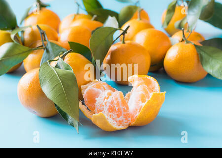 Ganz, frisch Mandarinen und Scheibe mit Blättern, die auf der blauen Tabelle. Gesunde Ernährung Konzept. Stockfoto