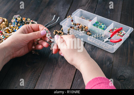 Frau machen Perlen Armband mit ihren Händen Closeup auf Holztisch Stockfoto