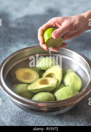 Hand zusammendrücken Kalk auf halbierte Avocados Stockfoto