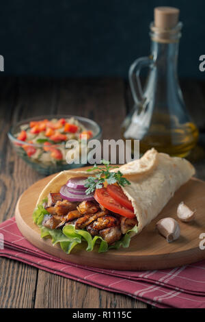 Döner liegt auf dem Schneidebrett. Shawarma mit Hähnchenfleisch, Zwiebeln, Salat liegt auf einem dunklen alten Holztisch. Stockfoto