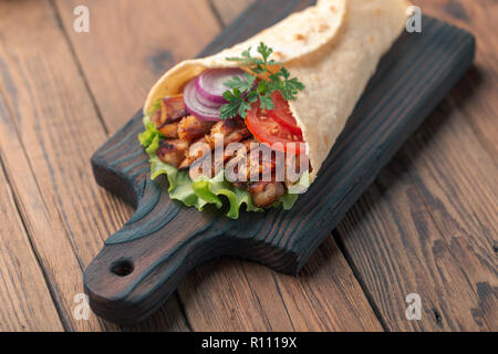 Döner liegt auf dem Schneidebrett. Shawarma mit Hähnchenfleisch, Zwiebeln, Salat liegt auf einem dunklen alten Holztisch. Stockfoto