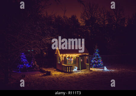 Bemalte gelben eigenes Kinderspielhaus im Haus Garten, mit Weihnachten dekoriert LED string Lichter draußen im Kalten winder Nacht. Dekorieren Stockfoto