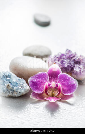 Ein rosa Orchidee Blüte mit Zen Steine und Amethyst Cluster und Cluster Blau Kristall auf hellen Hintergrund mit Wassertropfen. Alternative Medizin conce Stockfoto