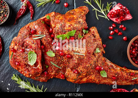 Ansicht von oben von Rohstoffen ganze Schulter von einem Lamm mariniert mit allen Gewürzen, Minze und Granatapfel Samen auf einen schwarzen Stein Fach, die geröstet werden, vie Stockfoto