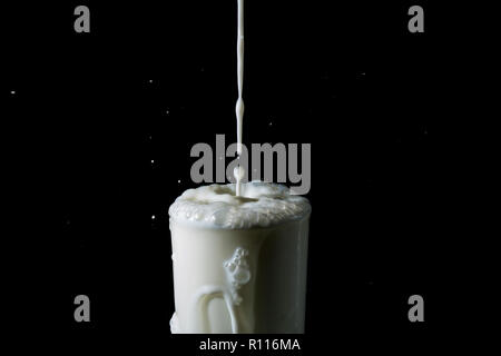 Splash von Milch im Glas, gießen Strom von Milch in einem Überquellenden Glas auf schwarzem Hintergrund Stockfoto