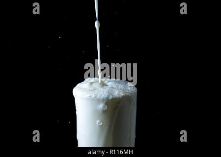 Splash von Milch im Glas, gießen Strom von Milch in einem Überquellenden Glas auf schwarzem Hintergrund Stockfoto