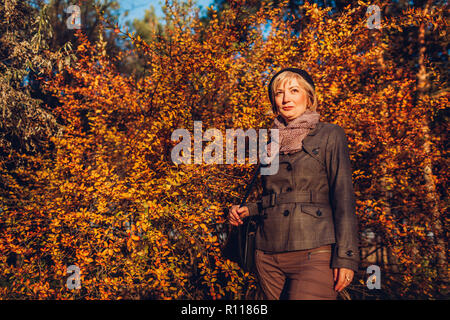 Frau mittleren Alters Wandern im Herbst Wald. Ältere Frau in stilvollen fallen Outfit mit Zubehör Stockfoto