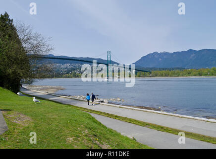 Menschen zu Fuß auf den Stanley Park Seawall in Vancouver, Kanada, mit Blick auf den Lion's Gate Bridge. Stockfoto