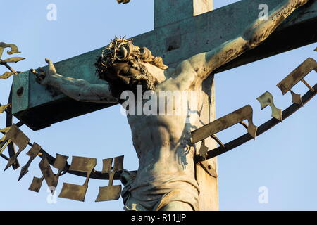 Schöne Jesus Christus Kreuzigung Bronzestatue bei Sonnenaufgang, den Statuen des Hl. Kreuz mit dem Kalvarienberg, Karlsbrücke, Prag, Tschechien, Sonnig Stockfoto