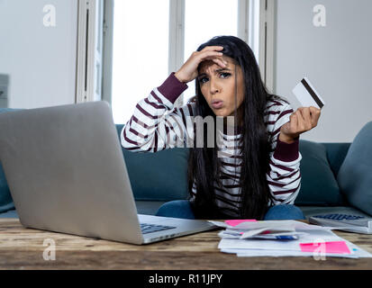 Attraktive junge Latin Frau verzweifelt und wütend mit Kreditkarte und Laptop Standortwahl auf dem Sofa zu Hause in der Kreditkarte Probleme Schulden online Zahlung online Stockfoto