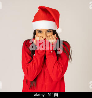 Schön und freundlich lächelnde junge Frau in Santa Hat und Red Pullover lächelnd verspielt und Holding Kopie Raum über grauer Hintergrund in frohe Weihnachten Stockfoto