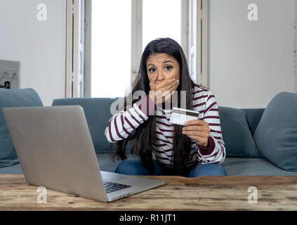 Attraktive junge Latin Frau verzweifelt und wütend mit Kreditkarte und Laptop Standortwahl auf dem Sofa zu Hause in der Kreditkarte Probleme Schulden online Zahlung online Stockfoto