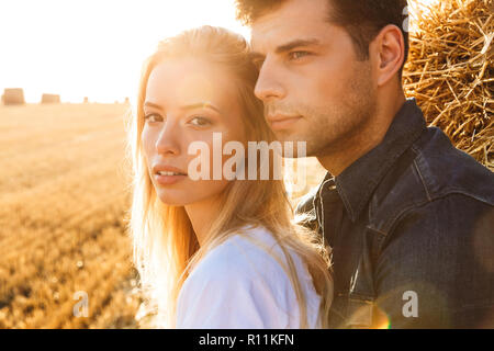 Image der Jungen stilvollen Mann und Frau gehen auf goldenen Feld und in der Nähe von großen Heuhaufen stehend Stockfoto