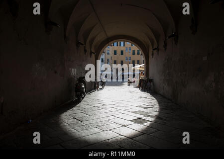 Am späten Nachmittag scheint die Sonne durch den Torbogen auf die Piazza dell'Anfiteatro jenseits, Lucca, Italien. Stockfoto