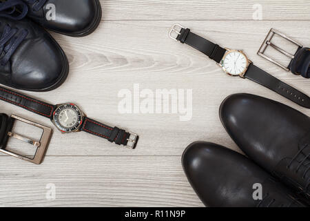 Zwei Paare von schwarzem Leder Männer Schuhe, zwei Gürtel für Männer und zwei Armbanduhren auf grau Holz- Hintergrund. Herren Accessoires. Ansicht von oben Stockfoto