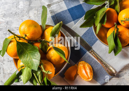 Flach auf reife Orangen Mandarinen Obst mit grünen Blättern, in Schalen, auf einem blauen und weißen Serviette, über weiße Holz- Hintergrund, kopieren. Stockfoto