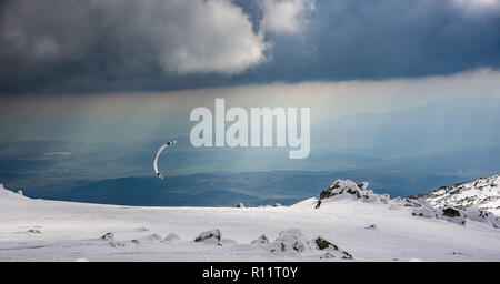 Dramatische Landschaft auf einem gefrorenen Berg - Parasailing unter den Strahlen der untergehenden Sonne mit der wunderschönen Kulisse auf Schnee und Fels Stockfoto