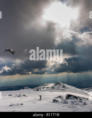 Dramatische Landschaft auf einem gefrorenen Berg - Parasailing unter den Strahlen der untergehenden Sonne mit der wunderschönen Kulisse auf Schnee und Fels Stockfoto