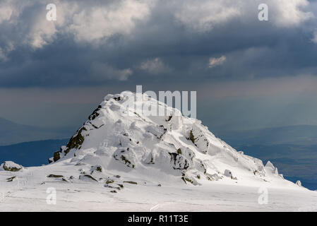 Dramatische Landschaft auf einem gefrorenen Berg - Parasailing unter den Strahlen der untergehenden Sonne mit der wunderschönen Kulisse auf Schnee und Fels Stockfoto