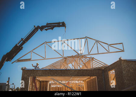 Builder Regie Kran Positionierung Rahmen über Gebäude Stockfoto