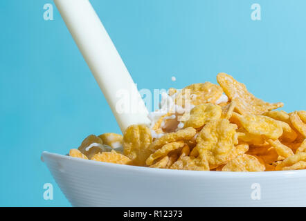 Milch stream Gießen in eine Schüssel mit gelben Flakes, Milch Spritzer auf einem hellblauen Hintergrund Stockfoto