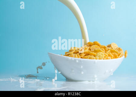 Milch stream Jet in eine Schüssel mit gelben Flocken gießen, Milch Spritzer auf einem hellblauen himmlischen Hintergrund Stockfoto