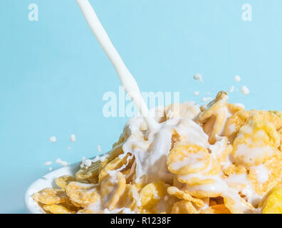 Milch stream Gießen in eine Schüssel mit gelben Flakes, Milch Spritzer auf einem hellblauen Hintergrund Stockfoto