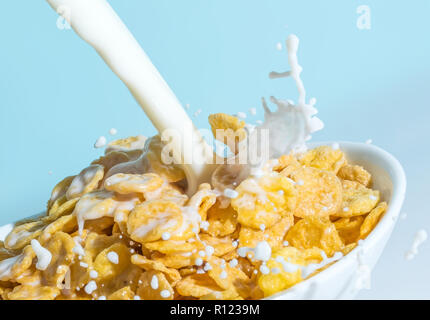 Milch stream Gießen in eine Schüssel mit gelben Flakes, Milch Spritzer auf einem hellblauen Hintergrund Stockfoto