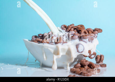 Milch stream jet Gießen in eine Schale mit Schokolade Flocken in der Form von Ringen, Spritzer von Milch auf einem hellblauen himmlischen Hintergrund Stockfoto