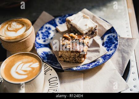 Scheibe einer Banane und Walnuss Kuchen auf eine Platte mit einem anderen Stück Kuchen. Es gibt zwei Tassen Kaffee neben dem Kuchen. Stockfoto