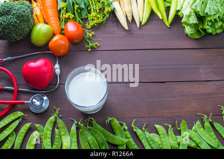 Gesundes Essen, Gemüse Bio im Holz- Hintergrund mit einem Glas Milch und Stethoskope mit roten Herzen, starken Körper Konzept. Stockfoto