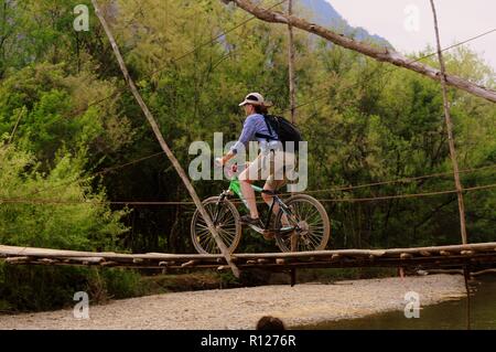 Sportliche Frau, Fahrten mit dem Fahrrad auf eine Holzbrücke über den Fluss Nom Song, Vang Vieng, Laos. Stockfoto