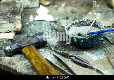 Blick von oben auf die verschiedenen Goldschmiede Werkzeuge auf den Schmuck am Arbeitsplatz. Desktop für Handwerk Schmuck machen mit professionellen Werkzeugen. Luftaufnahme von Werkzeugen über rustikal Hintergrund. Stockfoto