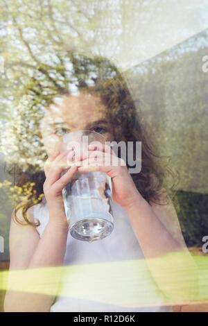 Junge Mädchen Trinkwasser durch Glas Fenster Stockfoto