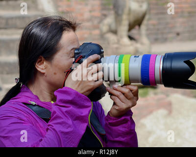 Chinesischen weiblichen Straße Fotograf macht ein Foto mit Ihrem Canon DSLR-Kamera und einem leistungsstarken Teleobjektiv. Stockfoto