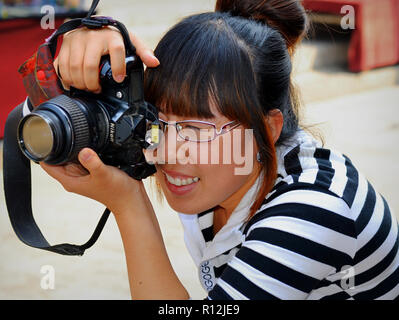 Junge chinesische weiblich Straße Fotograf macht ein Foto mit Ihrer Nikon Kamera. Stockfoto