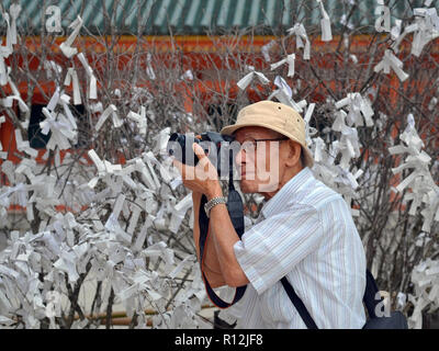 Älteren Japaner Straße Fotograf nimmt Fotos vor dem Baum des Glücks (OMIKUJI) an der Kyoto Heian Schrein. Stockfoto