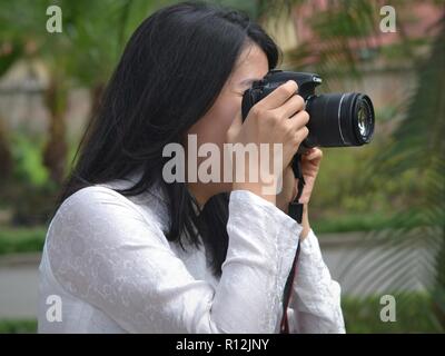 Junge vietnamesische Fotografin trägt ein weißes, traditionelles Kleid und hält eine Canon DSLR-Kamera mit beiden Händen. Stockfoto