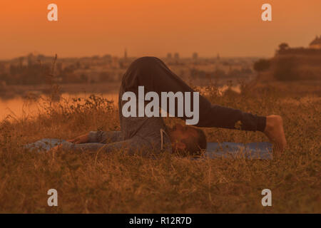 Man Yoga auf Sonnenuntergang mit Blick auf die Stadt, halasana/Pflug darstellen. Stockfoto