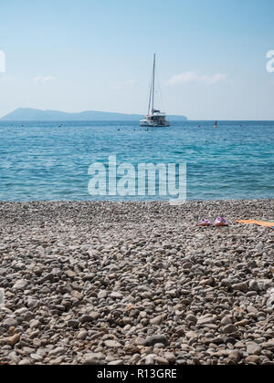 Kiesstrand an heißen Sommertagen auf der Insel Vis in Kroatien mit Segelboot im Hintergrund Stockfoto