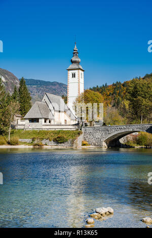 Gotische Kirche St. Johannes der Täufer und steinerne Brücke in Ribcev Laz, See Bohijn, Slowenien. Stockfoto