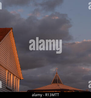 Am späten Abend Sonnenlicht leuchtet auf dem Dach eines Hauses und das Kreuz der Kirche gegen dunkle stürmische Wolken Stockfoto